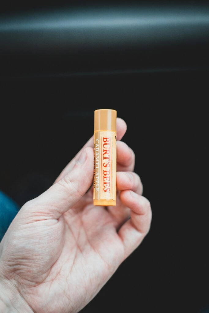 Close-up image of a hand holding Burt's Bees lip balm against a dark background.